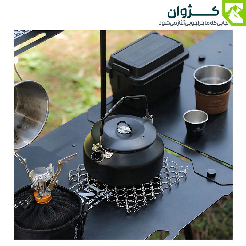 کتری کمپینگ BLACK DEER مدل K02 رنگ مشکی روی میز فلزی در کنار اجاق و لیوان‌های فضای باز