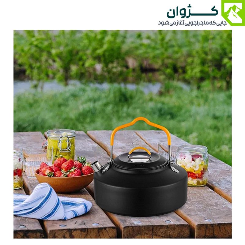کتری کمپینگ BLACK DEER مدل K02 رنگ مشکی روی میز چوبی در فضای پیک‌نیکی کنار رودخانه